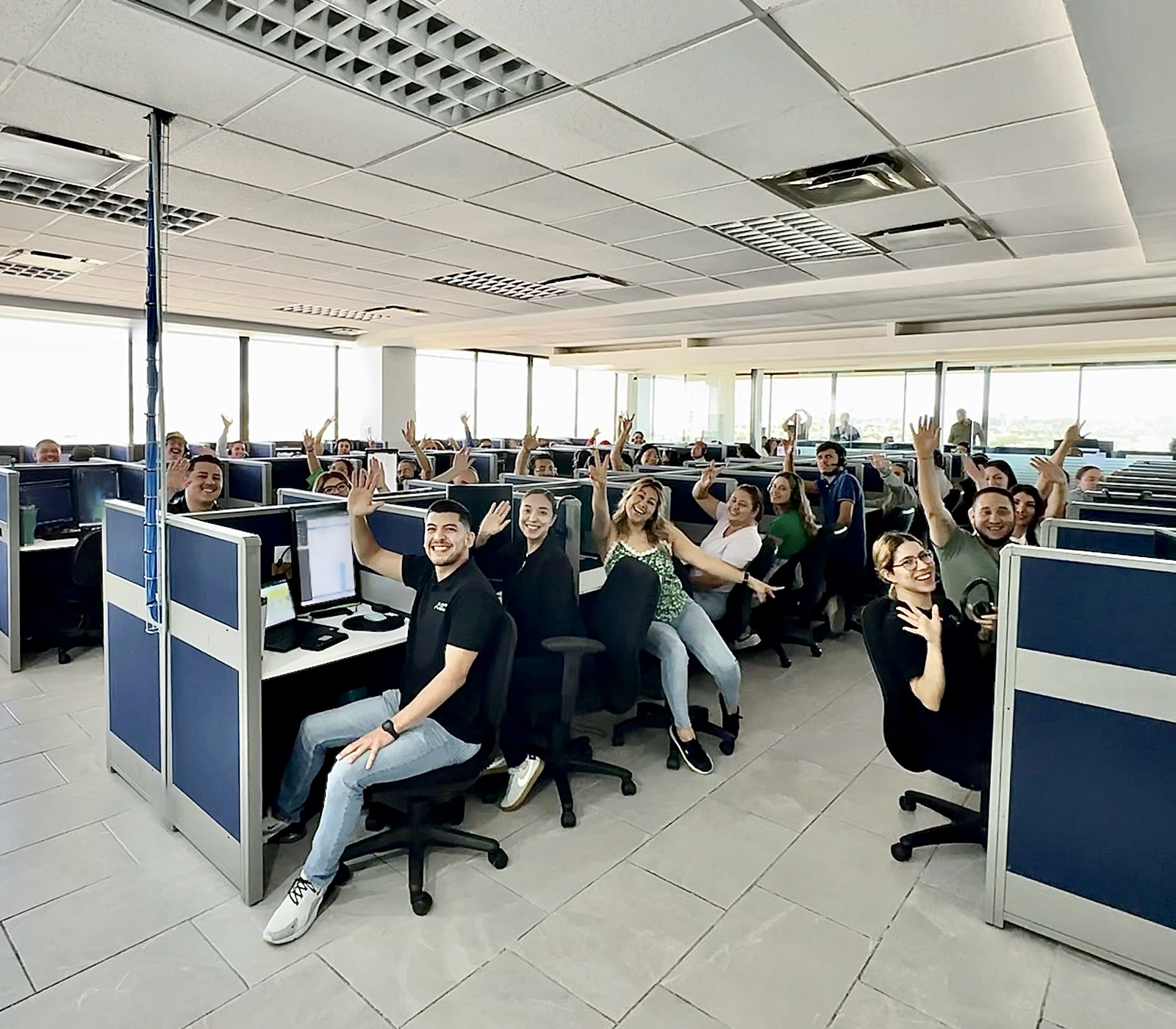 Alliance BPO Services team in Mexico, Offshore BPO Confidence Index 2023: Dozens of agents waving from their workstations in a large open-plan call center