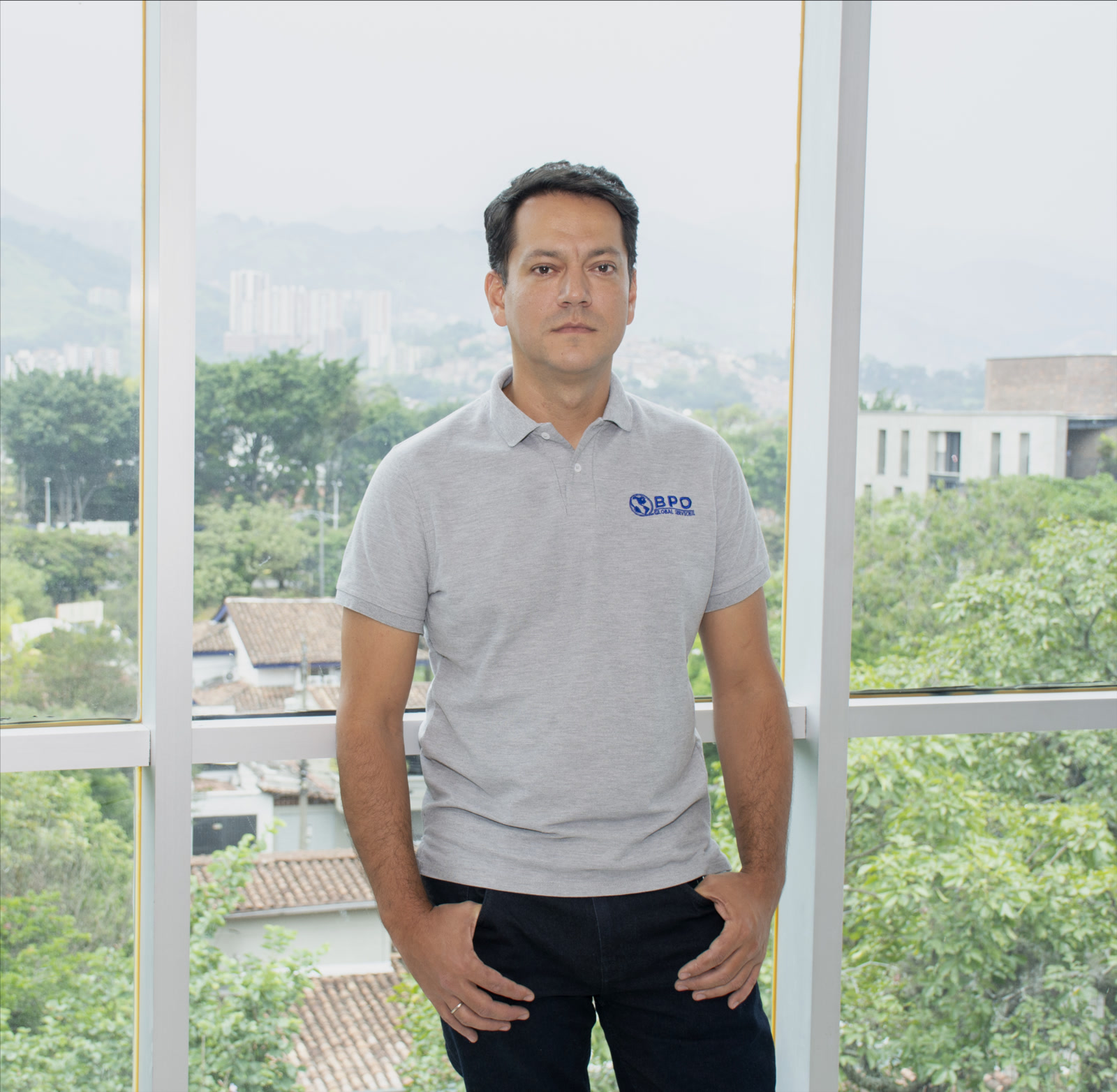 Andrés Arcila, CEO, BPO Global Services, Colombia, Offshore BPO Confidence Index 2023: Man in a gray polo shirt standing in front of floor-to-ceiling office windows with trees outside