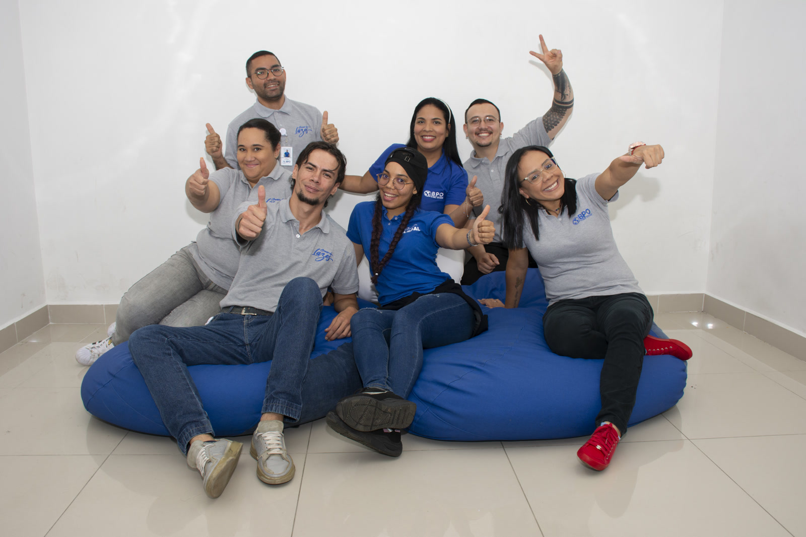 BPO Global Services team in Colombia, Offshore BPO Confidence Index 2023: Eight smiling employees in company polo shirts giving a thumbs up on a large blue beanbag