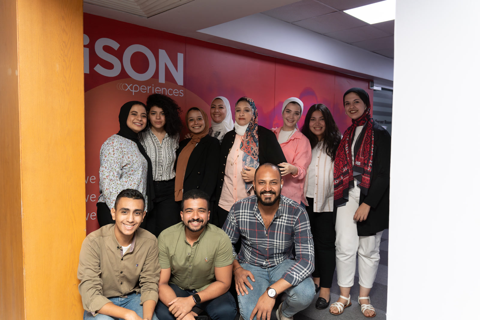iSON Xperiences team in Egypt, Offshore BPO Confidence Index 2023: About fourteen employees posing in front of an iSON Xperiences branded wall, three crouching in front