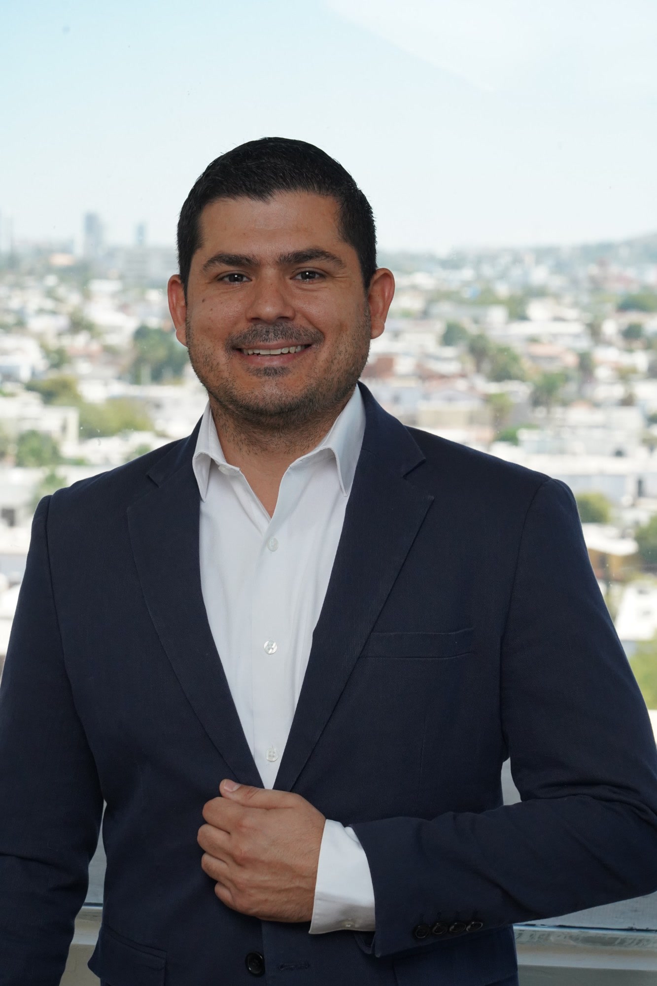 Juan Caire, CEO, Alliance BPO Services, Mexico, Offshore BPO Confidence Index 2023: Smiling man in a navy blazer and open-collared white shirt by a window overlooking the city
