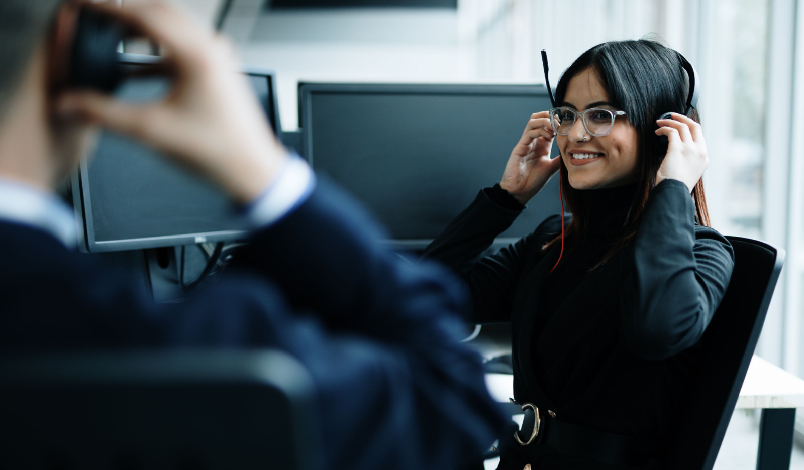 Sigma Connected team in South Africa, Offshore BPO Confidence Index 2023: Agent in a headset smiling at her computer while a colleague adjusts his headset in the foreground