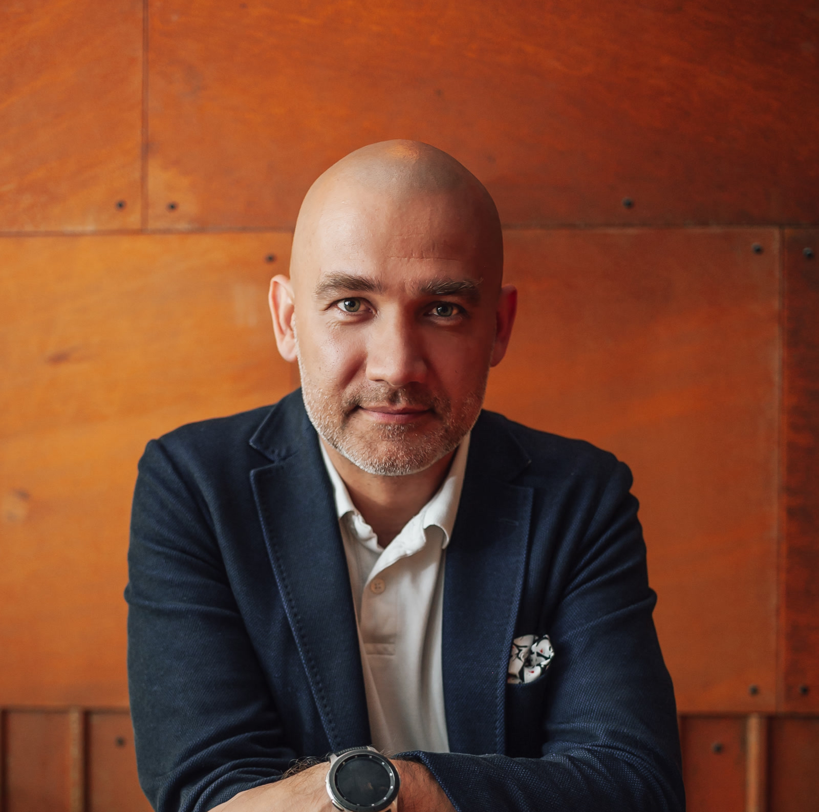 Wiktor Doktór, CEO, Pro Progressio, Poland, Offshore BPO Confidence Index 2023: Bald man with a short beard in a dark jacket and white shirt against an orange wall