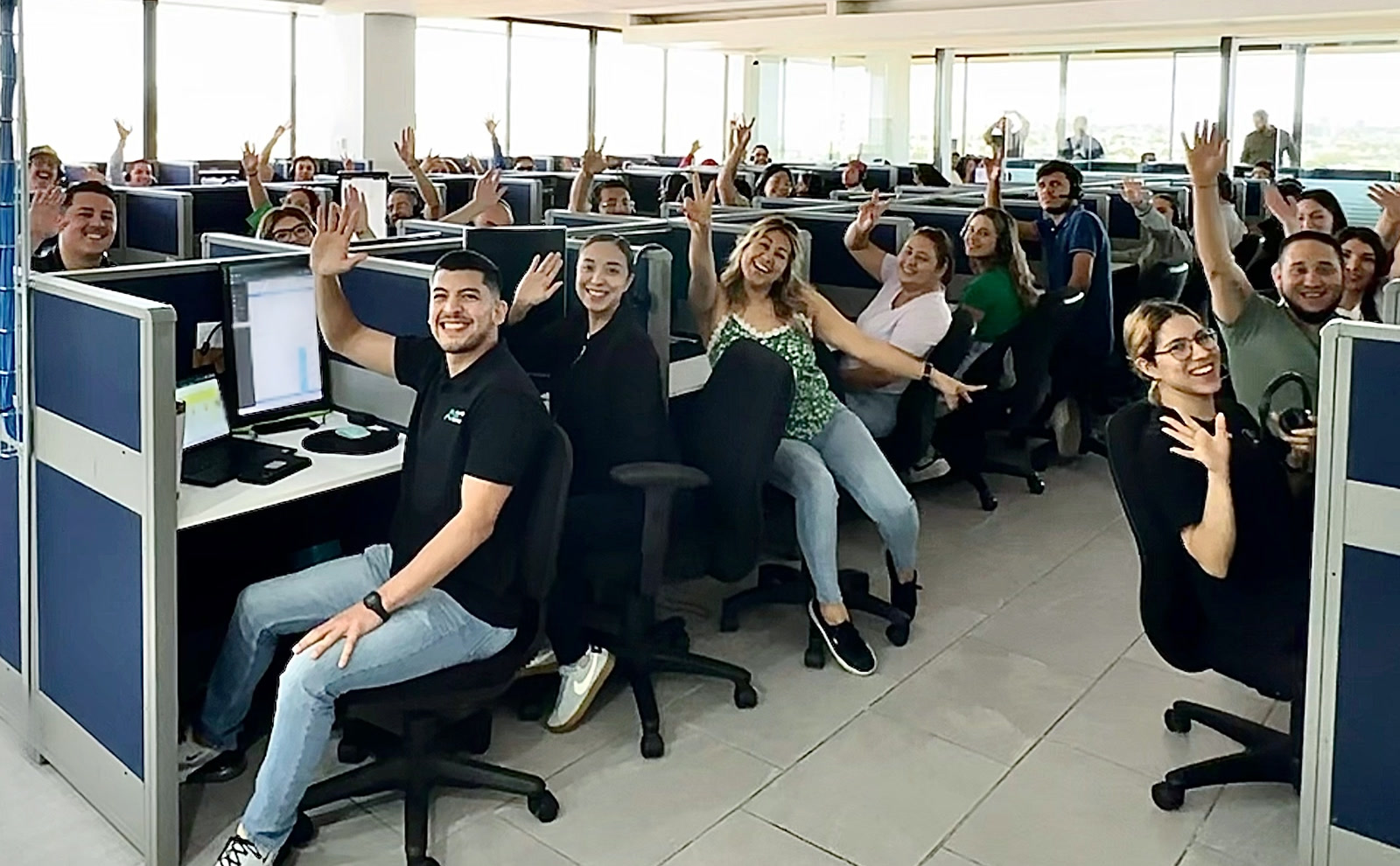 Alliance BPO Services team in Mexico, Offshore BPO Confidence Index 2024: About two dozen contact center employees smiling and waving from desks in a bright open-plan office