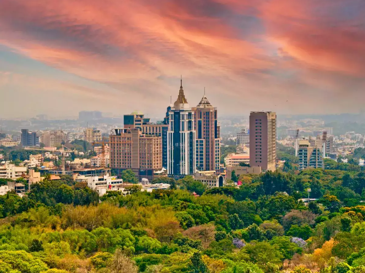 Skyline of Bengaluru, India under an orange and pink sky, with high-rise towers above green trees. India, Offshore BPO Confidence Index 2024