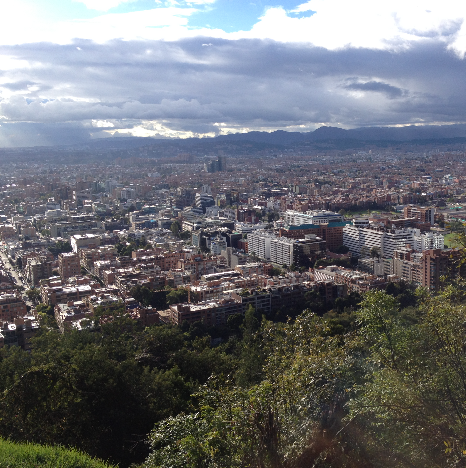 Aerial view of Bogota, Colombia with dense city blocks, tall office towers, and mountains under cloudy skies. Colombia, Offshore BPO Confidence Index 2024
