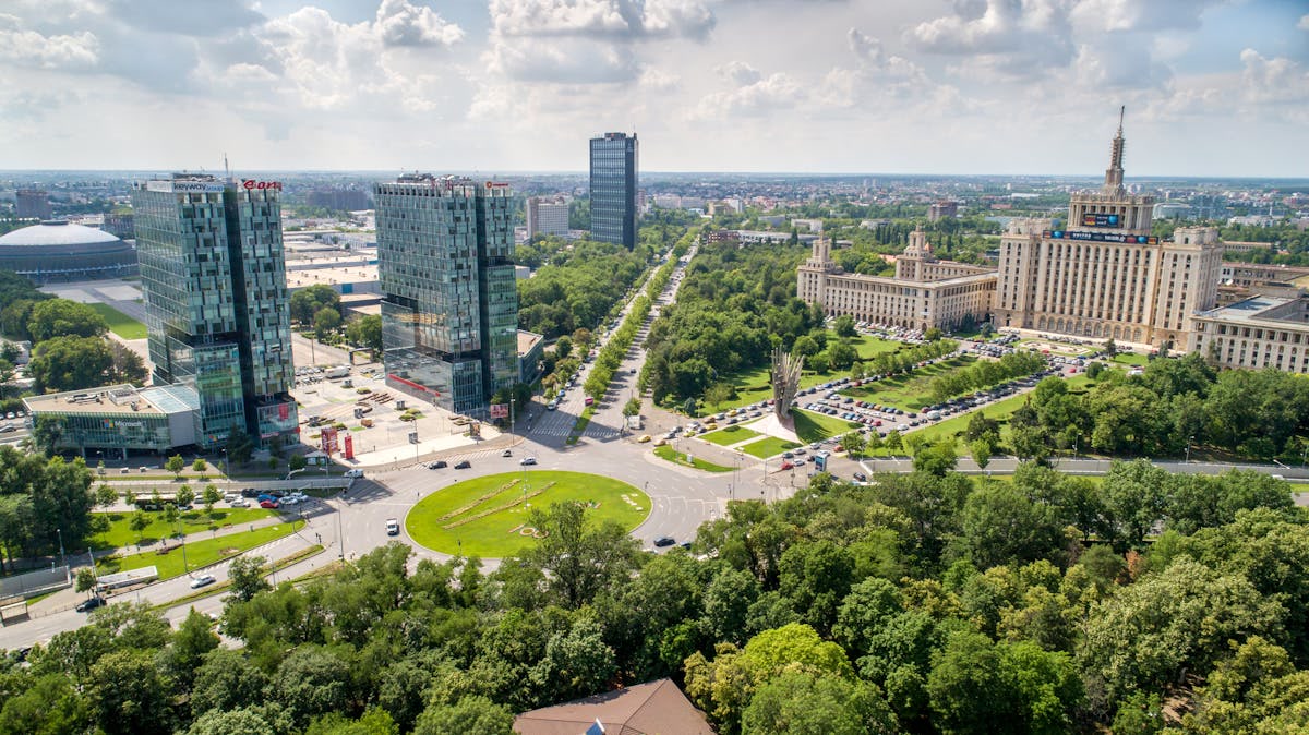 Aerial view of Bucharest, Romania, with glass office towers, a green roundabout, and a tree-lined boulevard. Romania, Offshore BPO Confidence Index 2024