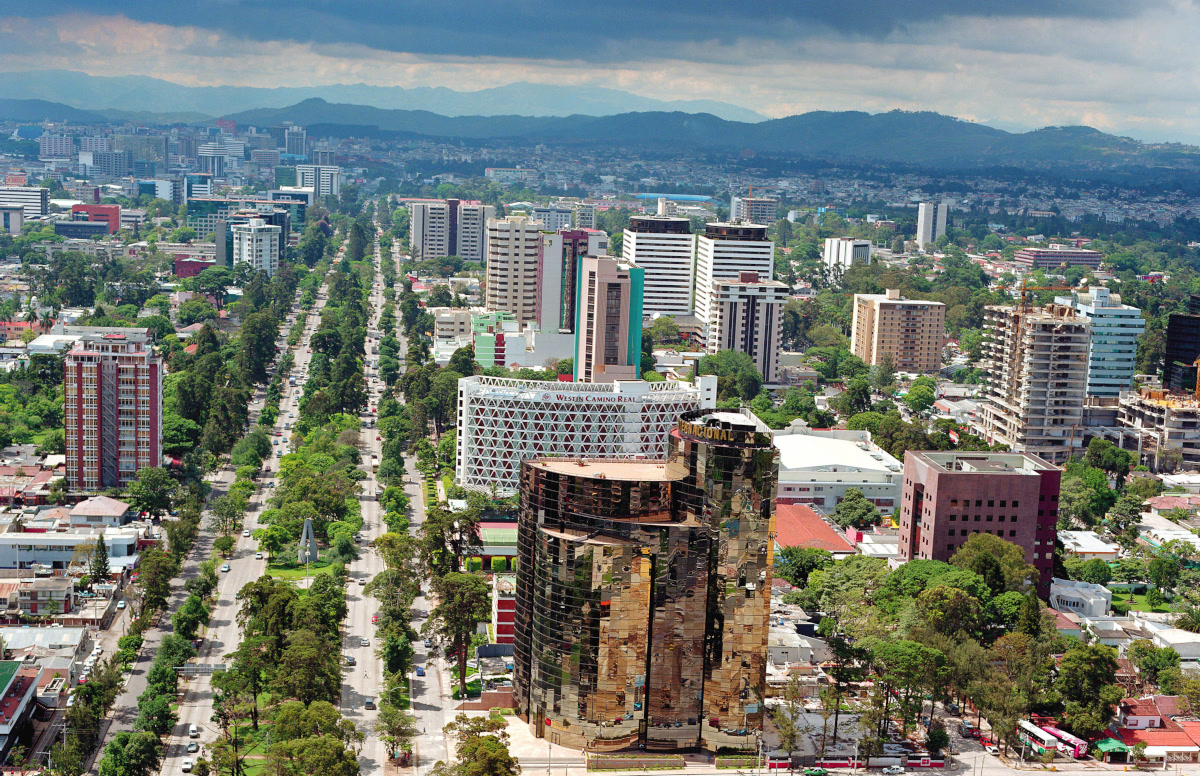 Aerial view of Guatemala City, Guatemala, with a tree-lined avenue, a mirrored tower, and distant mountains. Guatemala, Offshore BPO Confidence Index 2024