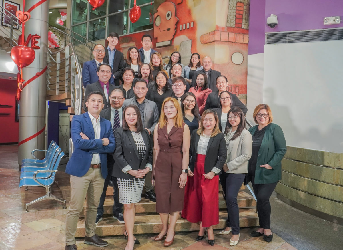 Inspiro Philippines team, Offshore BPO Confidence Index 2024: Roughly thirty people in business attire posing on stairs beneath a large painted mural in a lobby