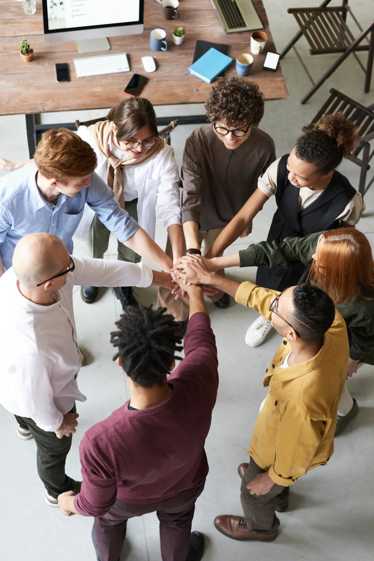 Overhead view of about ten people stacking hands together in a circle above a wooden desk. Introduction, Offshore BPO Confidence Index 2024