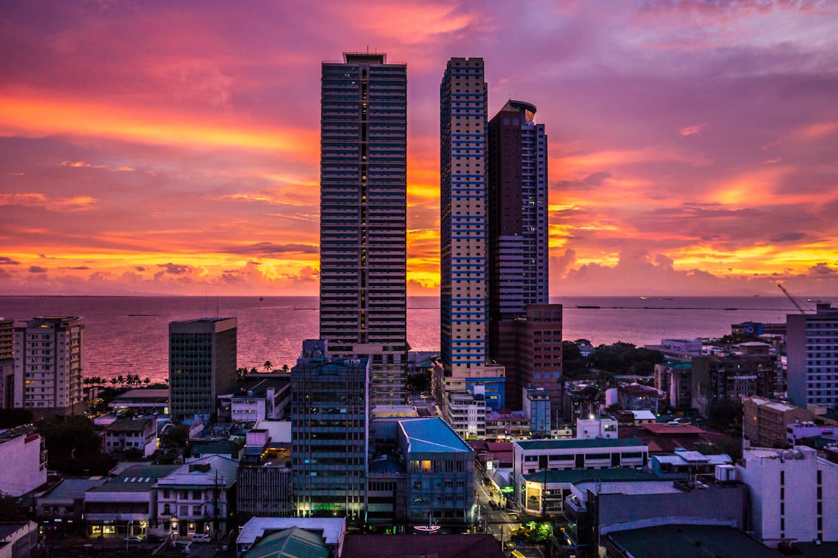 Sunset over Manila, Philippines, with two tall high-rise towers and the sea under a purple and orange sky. Philippines, Offshore BPO Confidence Index 2024
