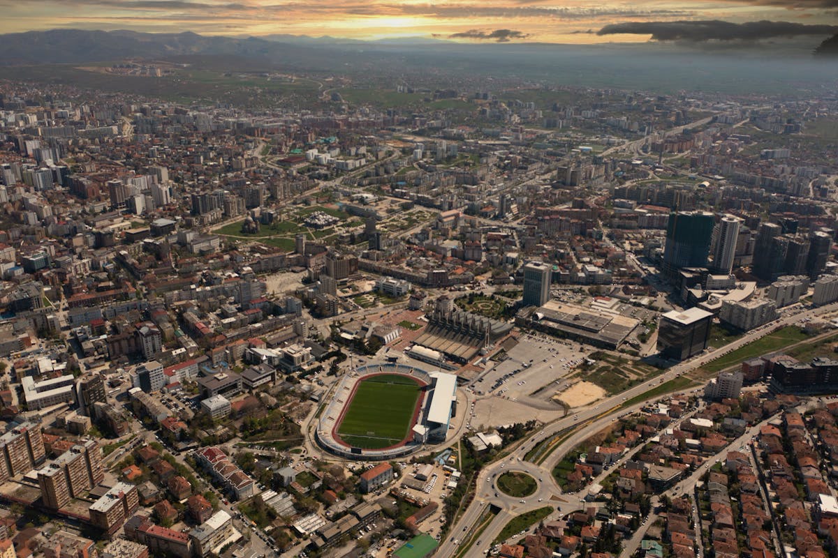 Aerial view of Pristina, Kosovo at sunset, with apartment blocks and a stadium with a green field. Kosovo, Offshore BPO Confidence Index 2024