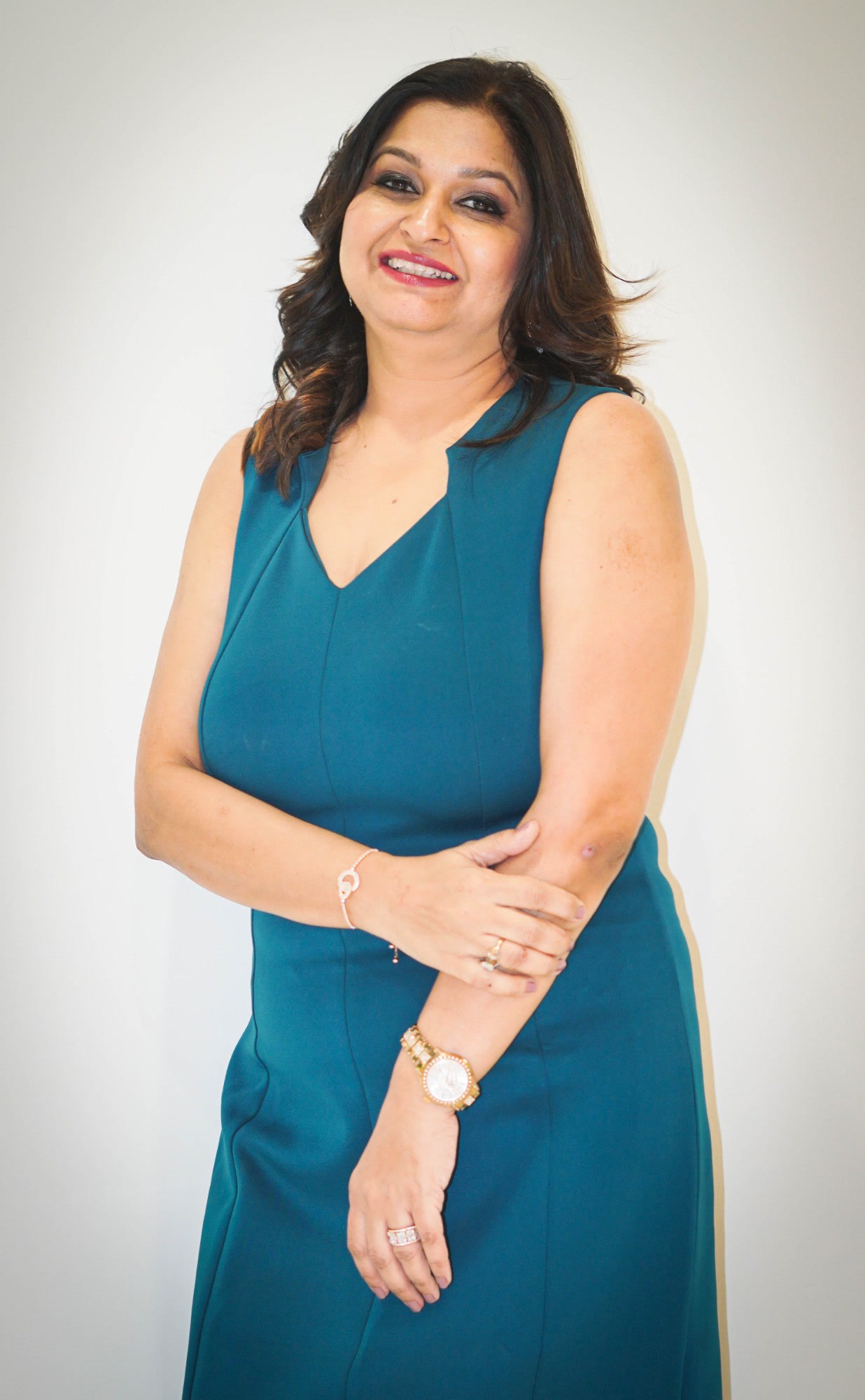 Sapna Bhambani, Senior VP of Operations, TaskUs India, Offshore BPO Confidence Index 2024: Smiling woman with wavy shoulder-length brown hair in a teal sleeveless dress against a plain light background