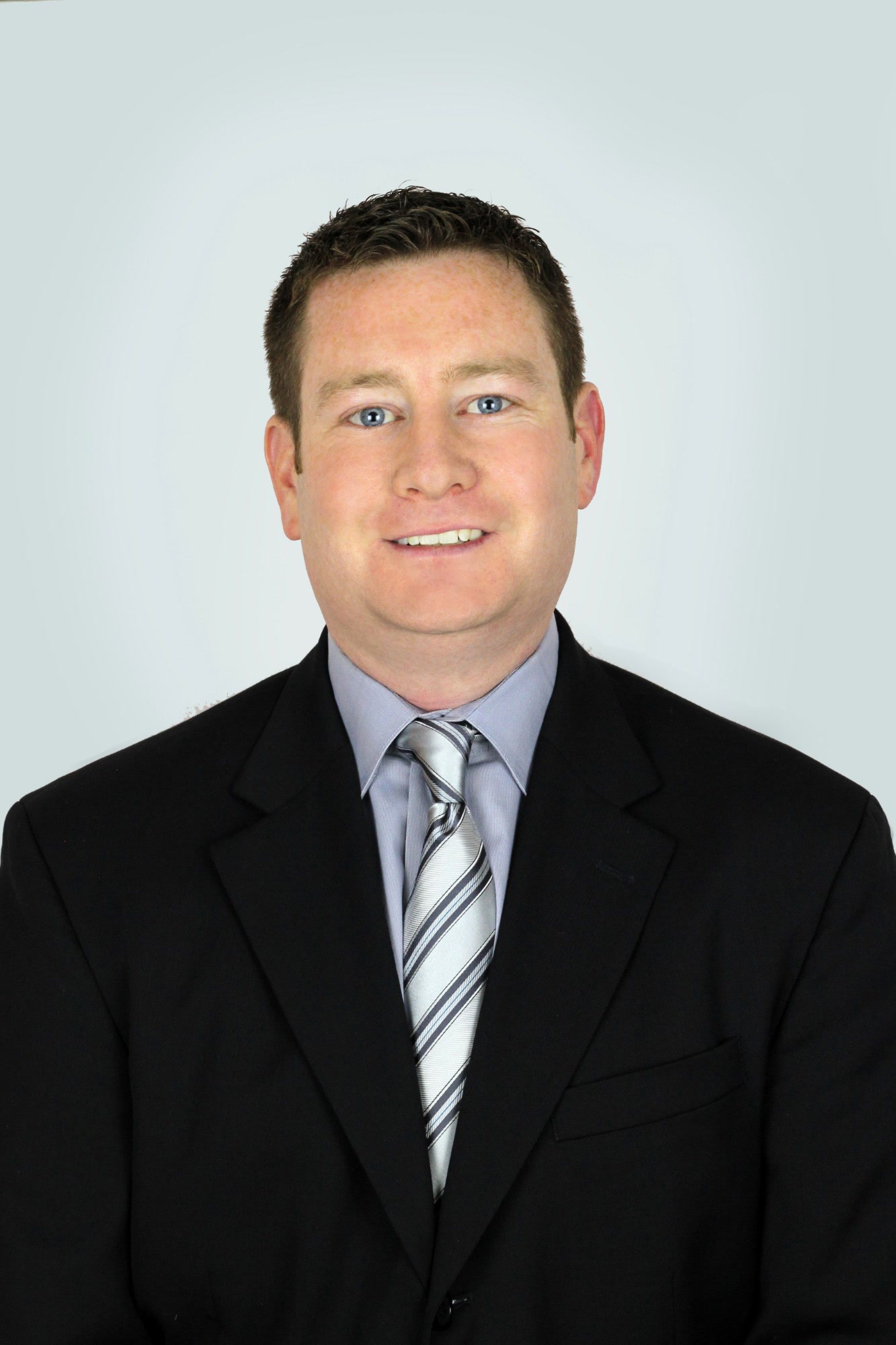 Scott Newman, Chief Strategy Officer, OneSource, Belize, Offshore BPO Confidence Index 2024: Smiling man in a dark suit and striped silver tie against a plain light gray background