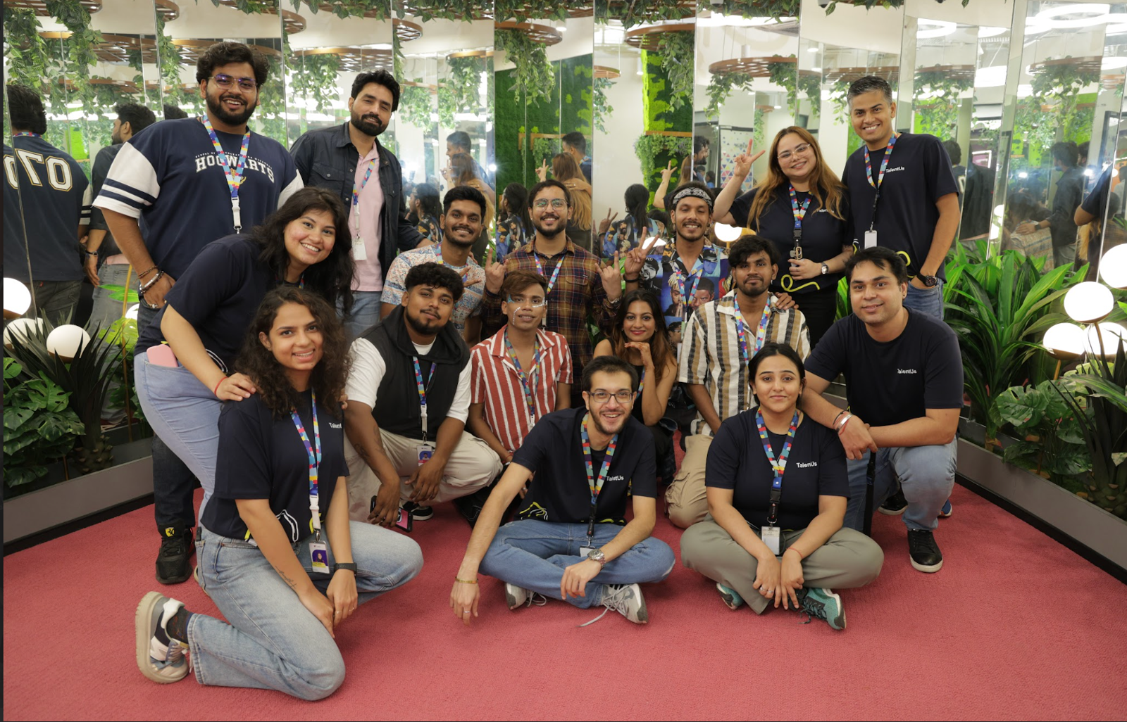 TaskUs India team, Offshore BPO Confidence Index 2024: About sixteen smiling employees posing on a red carpet in a mirrored room with plants