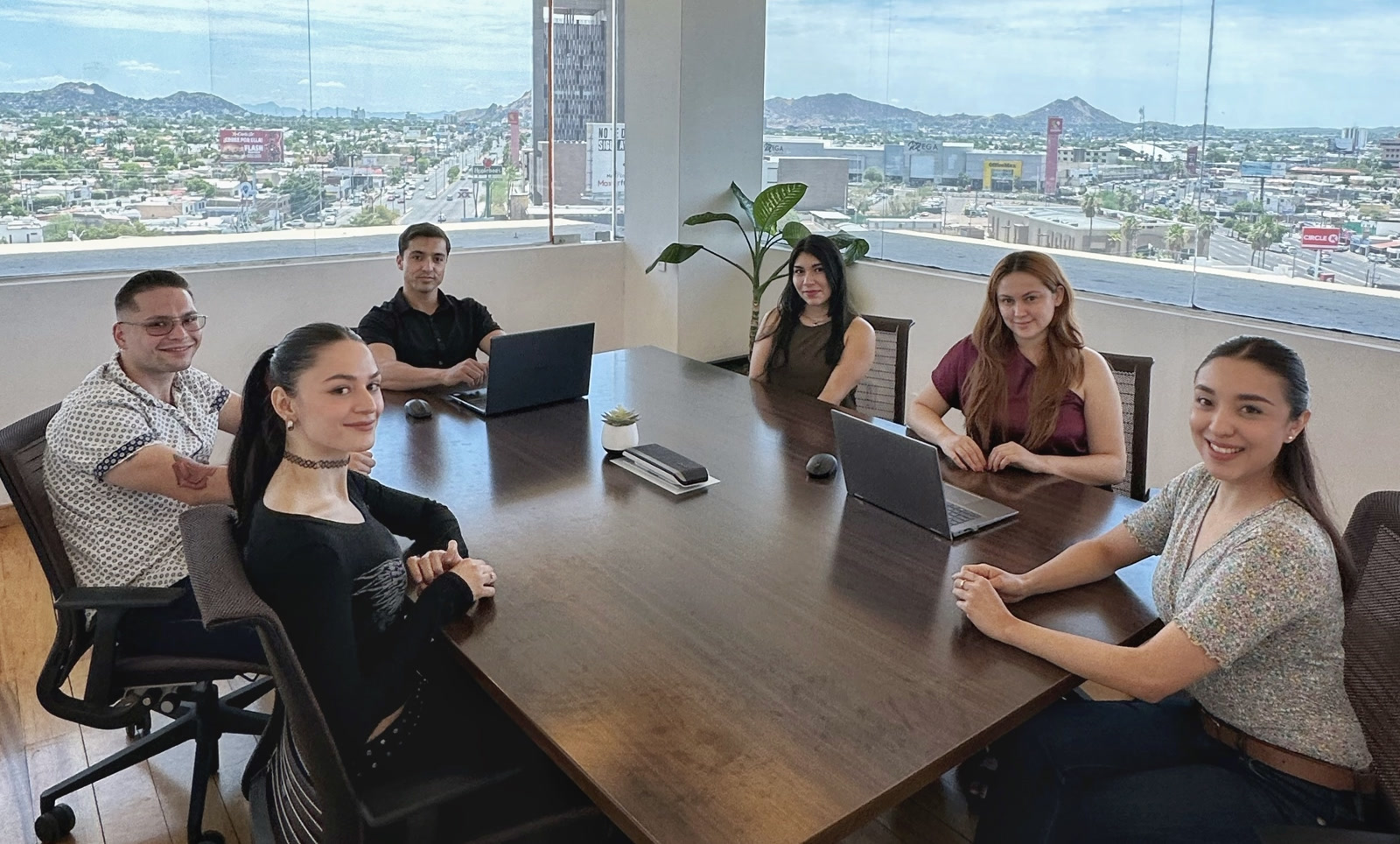 Alliance BPO Services team in Mexico, Offshore CX Confidence Index 2025: Six colleagues seated around a dark wooden conference table, laptops open, with a city view through large windows