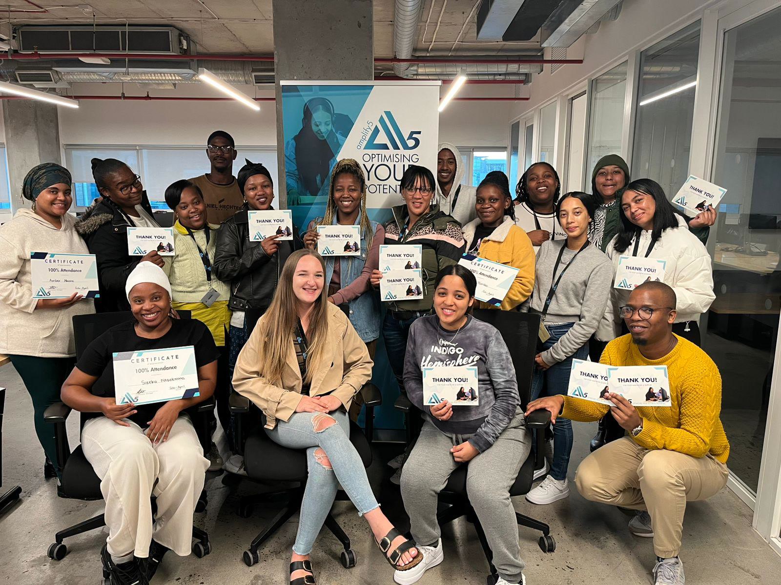 Amplify5 team in South Africa, Offshore CX Confidence Index 2025: About twenty employees hold certificates and thank-you cards in an office beside a blue banner