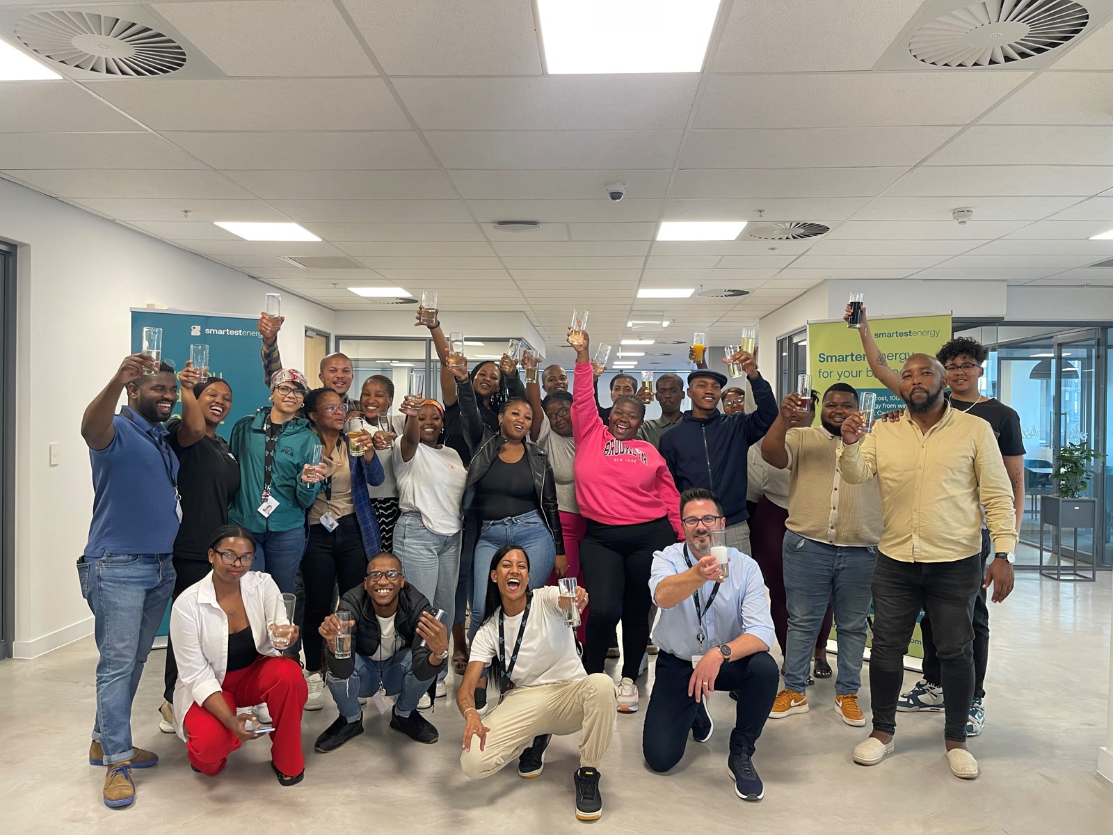 Amplify5 team in South Africa, Offshore CX Confidence Index 2025: About twenty employees raising glasses in a toast in a bright open office with green banners