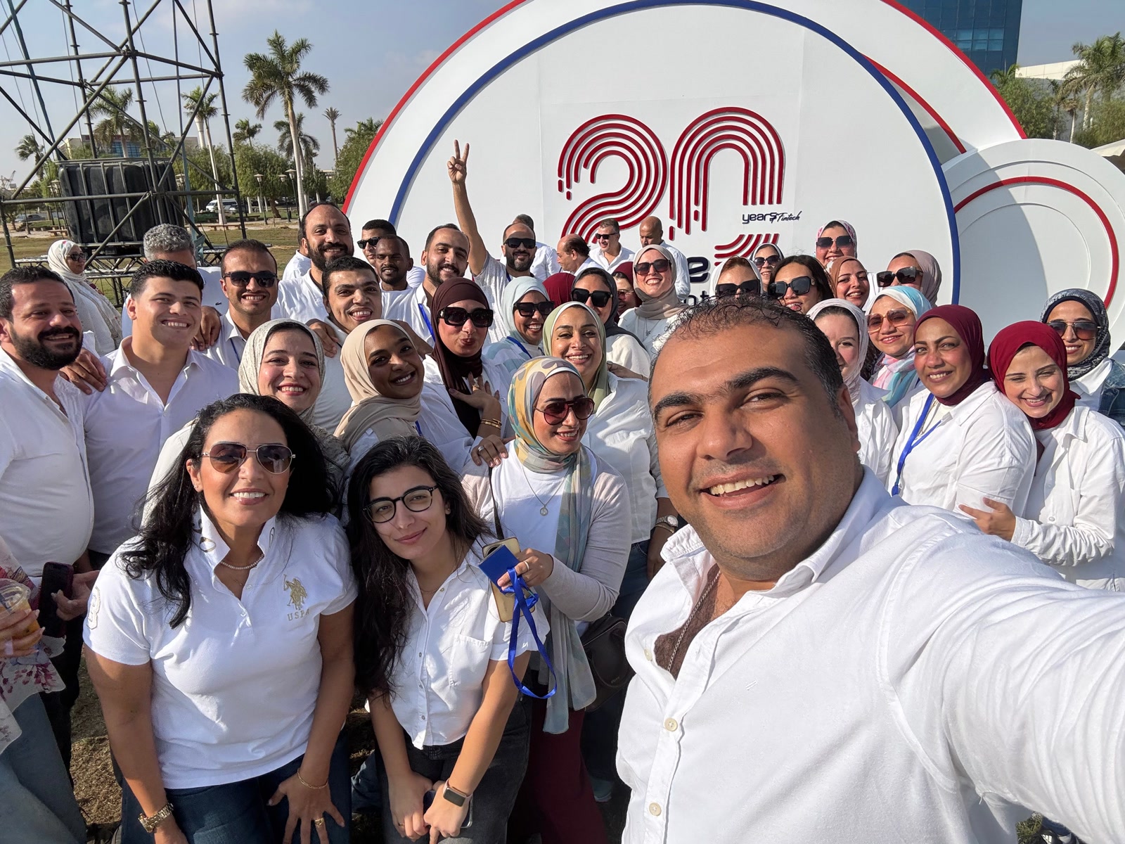 eNable Outsourcing team in Egypt, Offshore CX Confidence Index 2025: About forty employees in white shirts take a selfie in front of a 20-year anniversary sign outdoors