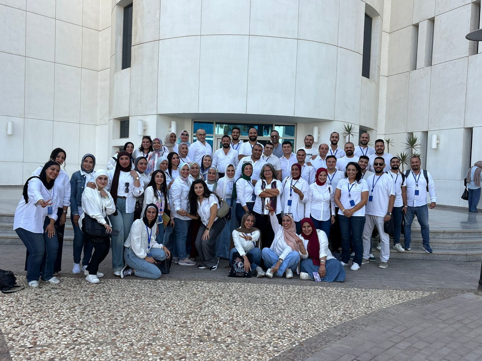 eNable Outsourcing team in Egypt, Offshore CX Confidence Index 2025: About fifty employees in white shirts posing outside a large cream stone building with steps