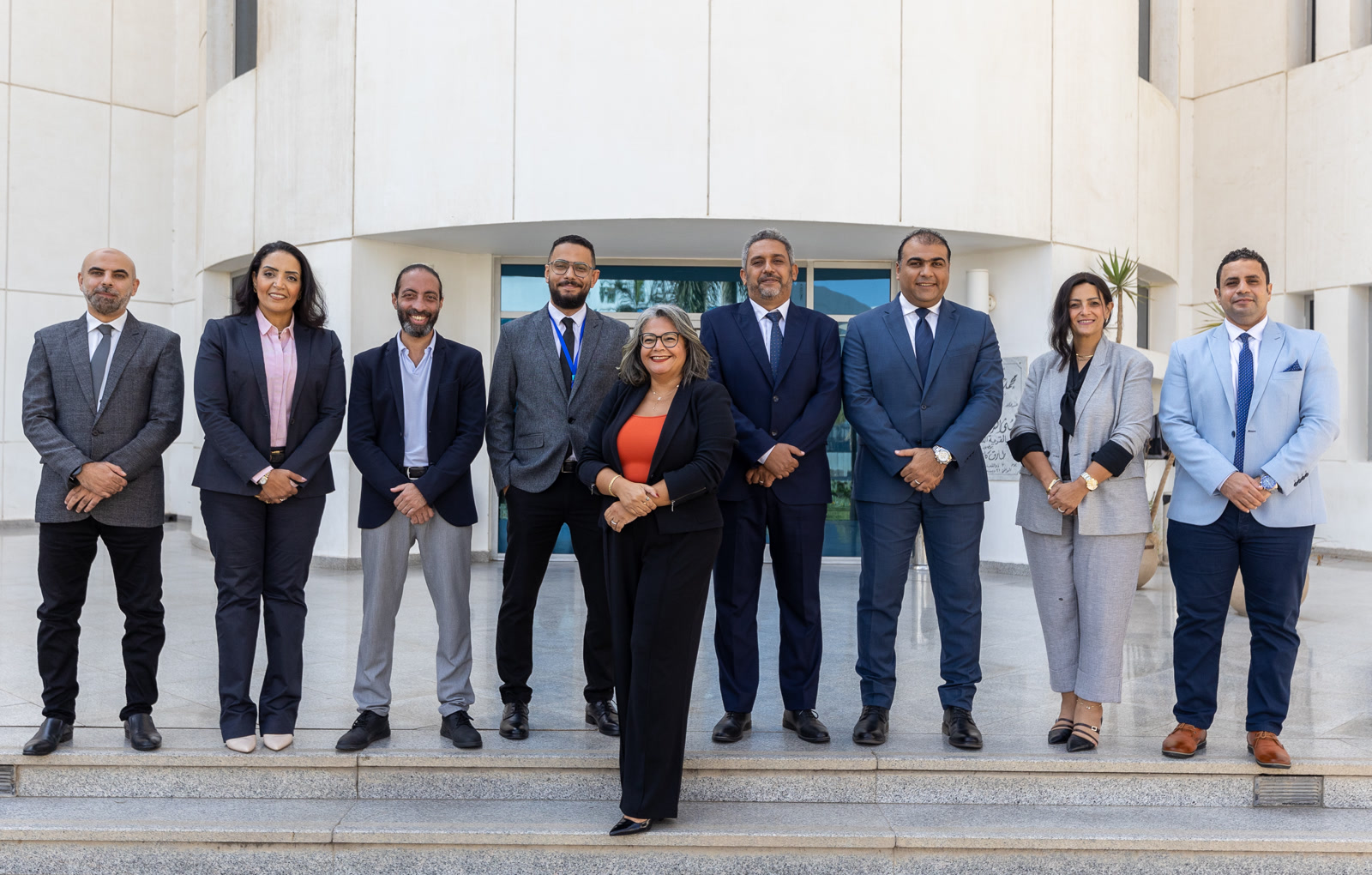 eNable Outsourcing team in Egypt, Offshore CX Confidence Index 2025: Nine people in business attire standing in a row in front of a white curved building