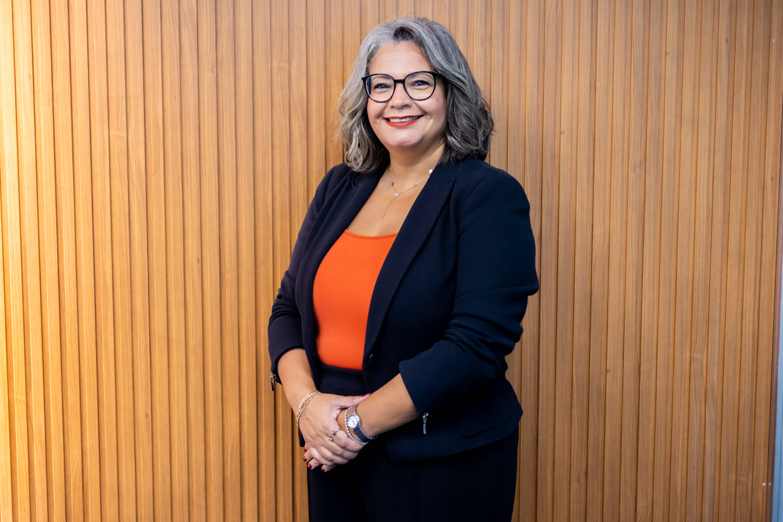 Maggi Dewedar, CEO, eNable Outsourcing, Egypt, Offshore CX Confidence Index 2025: Woman with gray hair and glasses in a black blazer and orange top before a wood-slat wall
