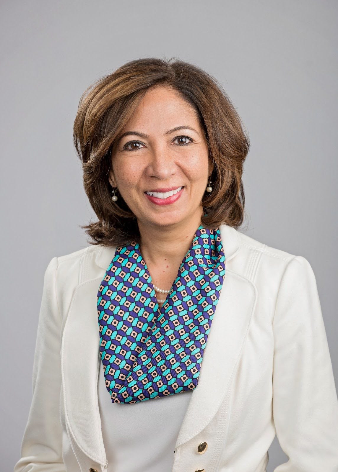 Vidya Ravichandran, Chief Executive Officer, UnifyCX, India, Offshore CX Confidence Index 2025: Smiling woman with wavy brown hair in a white blazer and patterned scarf against a gray backdrop